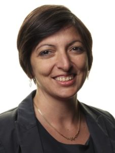 Prof Bruno has short dark hair and a grey jacket, and she is smiling.