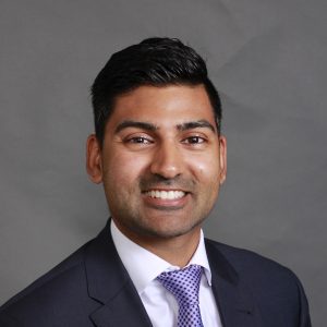 Portrait of Hari smiling at the camera. He has short black hair, brown eyes and a lovely smile. He is wearing a light purple tie, white shirt and dark suit.